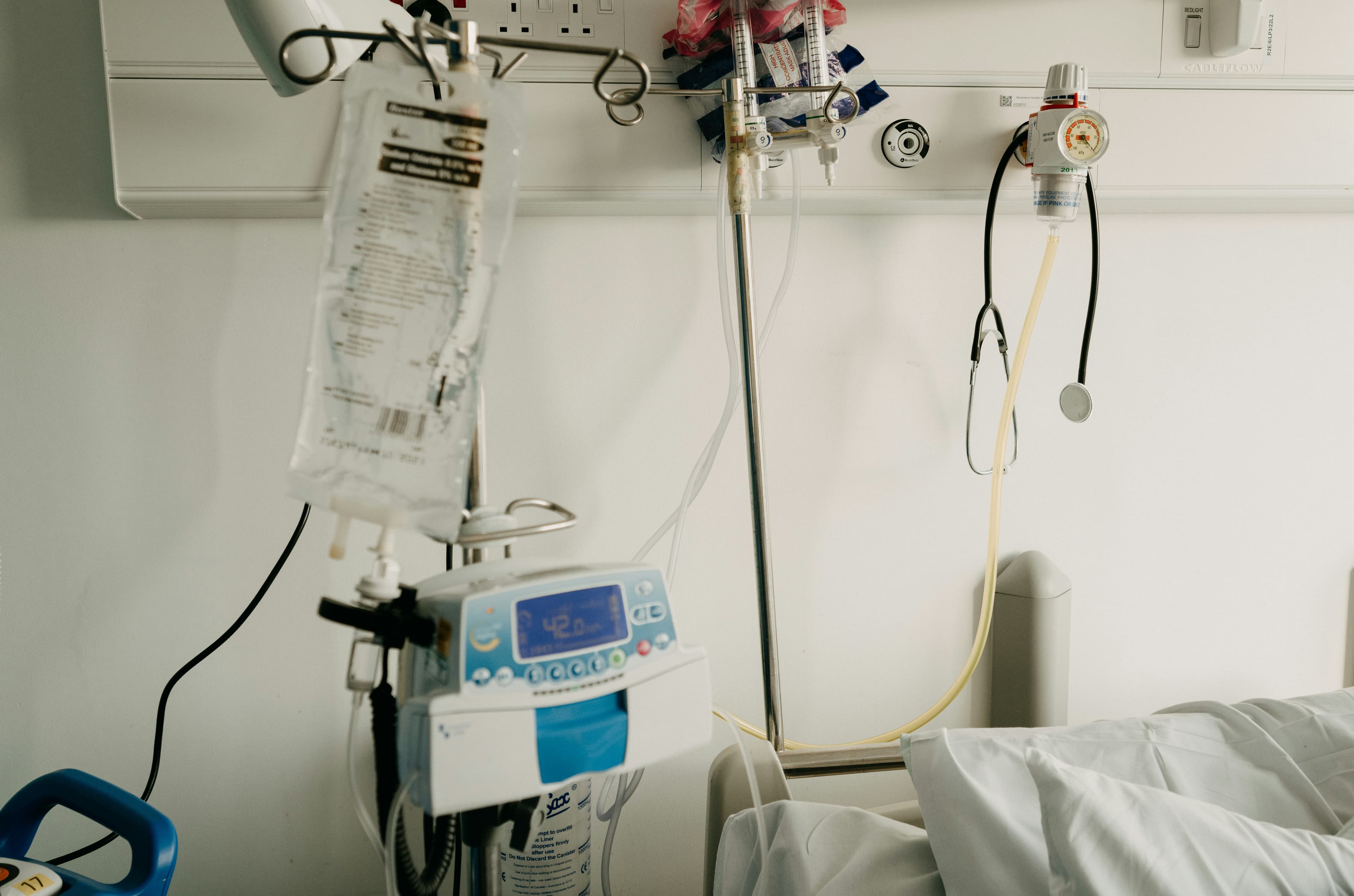 Bolsa de suero IV con bomba de infusión y estetoscopio en cabecera hospitalaria