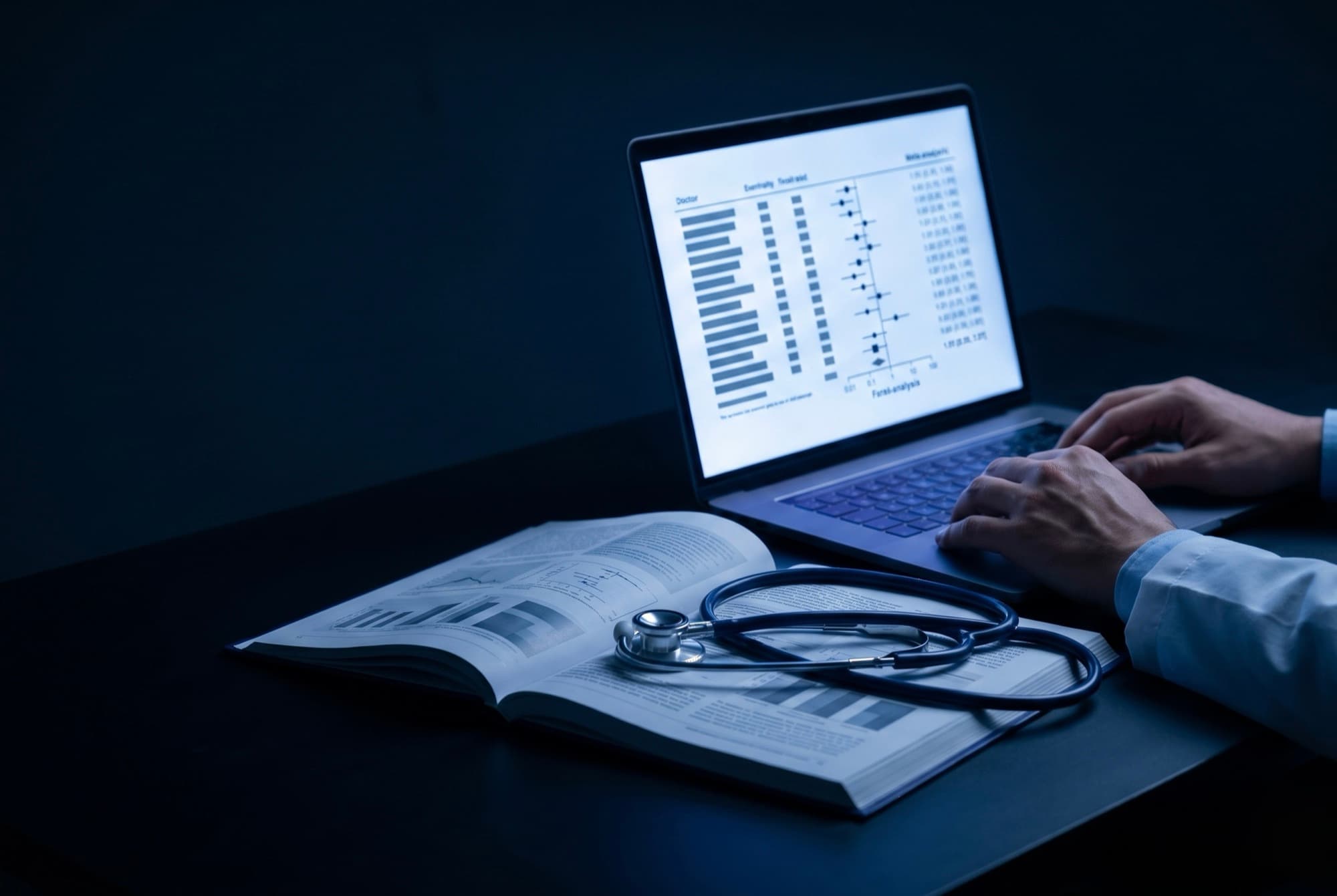 Laptop mostrando un forest plot de metaanalisis junto a un libro de medicina