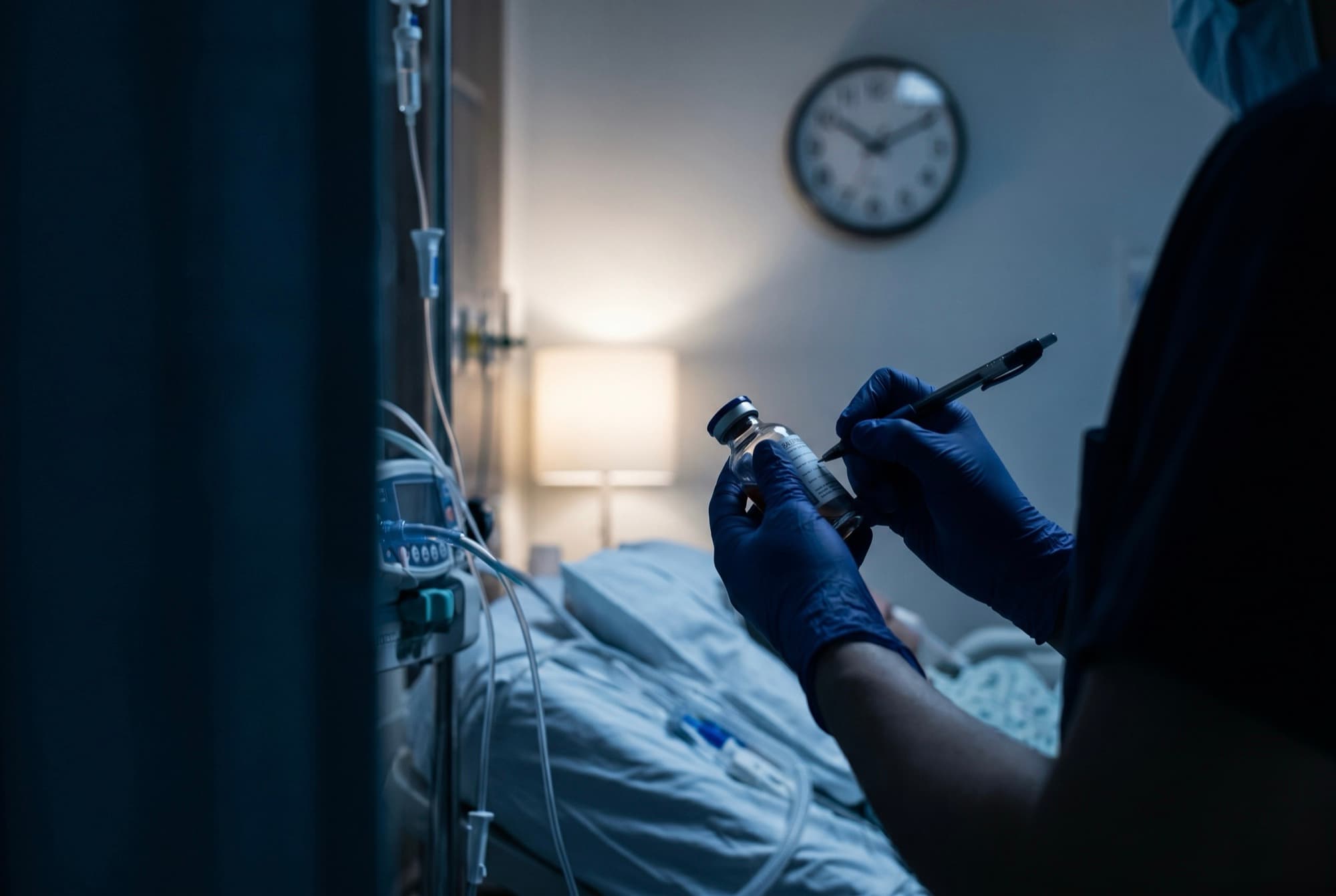 Mano enguantada preparando una muestra junto a la cama, con un reloj de pared al fondo — la primera hora de la sepsis